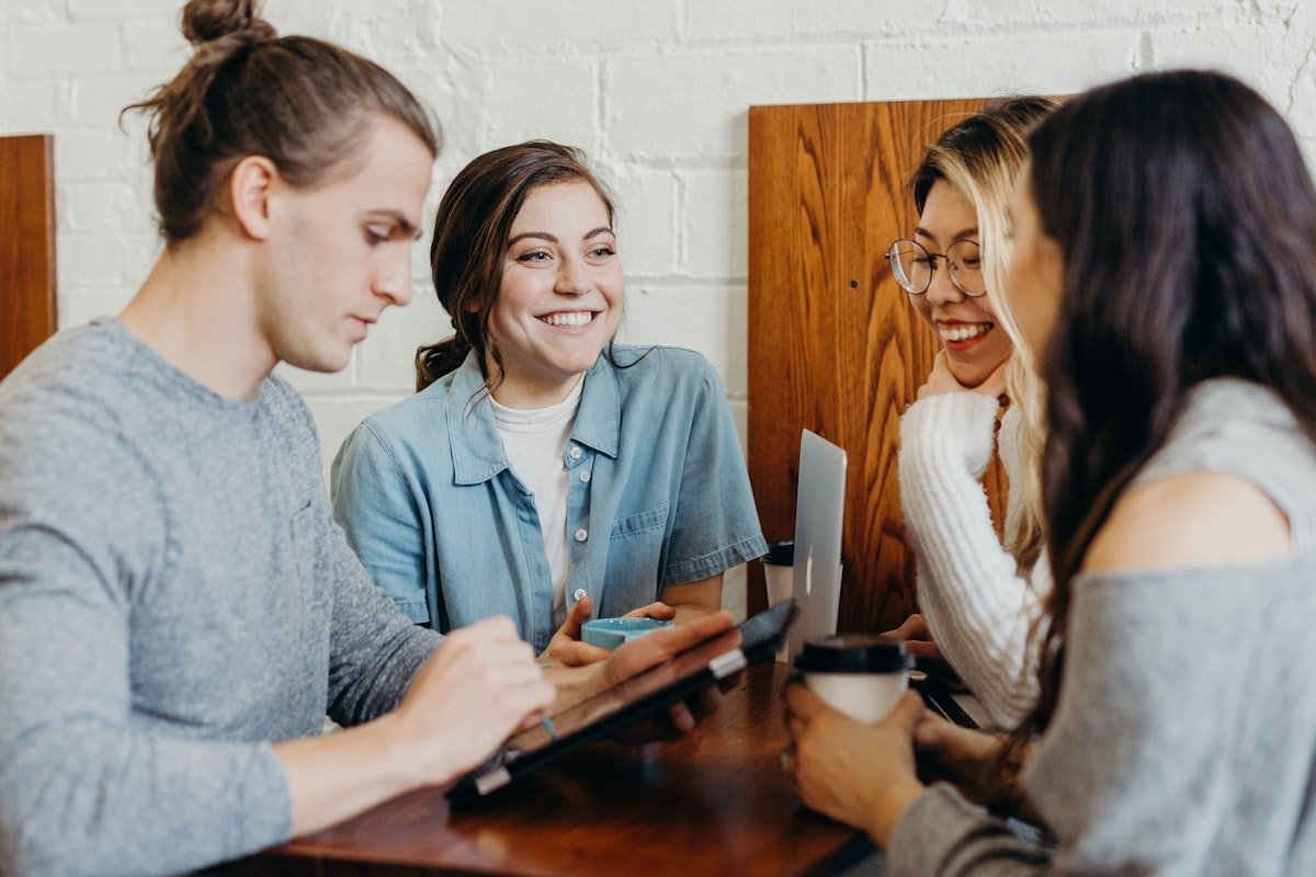 Four young adults talking and laughing together around a table with a tablet