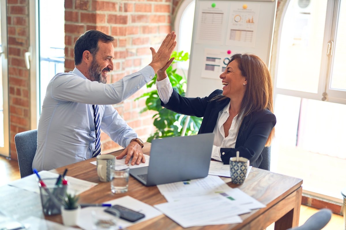 Two professional colleagues celebrating a success at their office desk